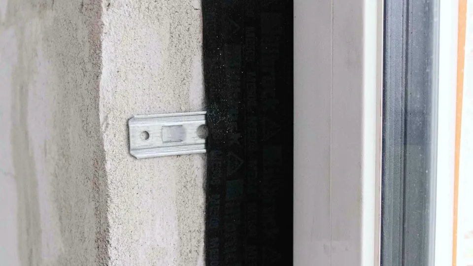 Detalle de una ventana en obra: escuadra metálica de anclaje y membrana negra de estanqueidad entre el muro y el marco