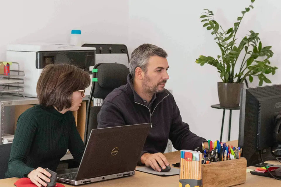 Una arquitecta y un arquitecto trabajando con sus ordenadores en la mesa del estudio