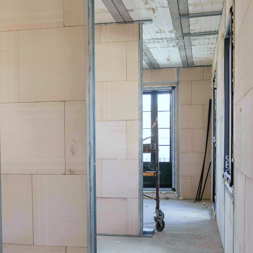 Interior de una vivienda en obra con trasdosados de paneles, perfilería metálica y un andamio junto a una puerta balconera